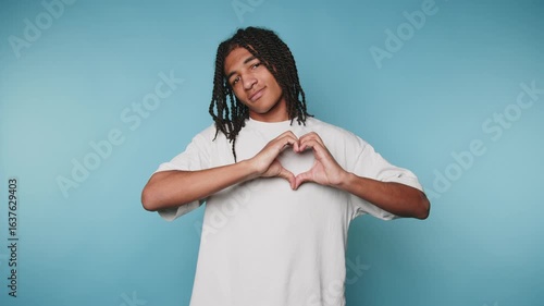 footage of young man expresses love and positivity by forming a heart shape with his hands on light blue background