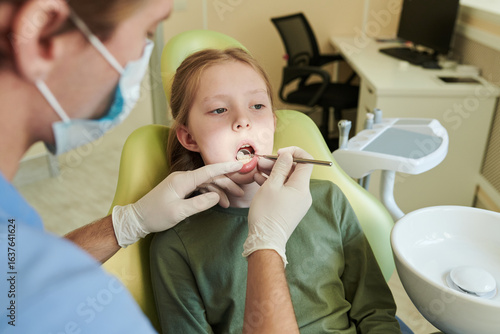 Obraz na płótnie Caucasian girl child sitting in dental chair receiving oral examination from mal