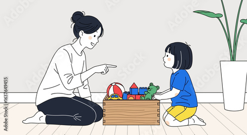 A mother points while interacting with her child, who is holding a toy near a wooden toy chest.
