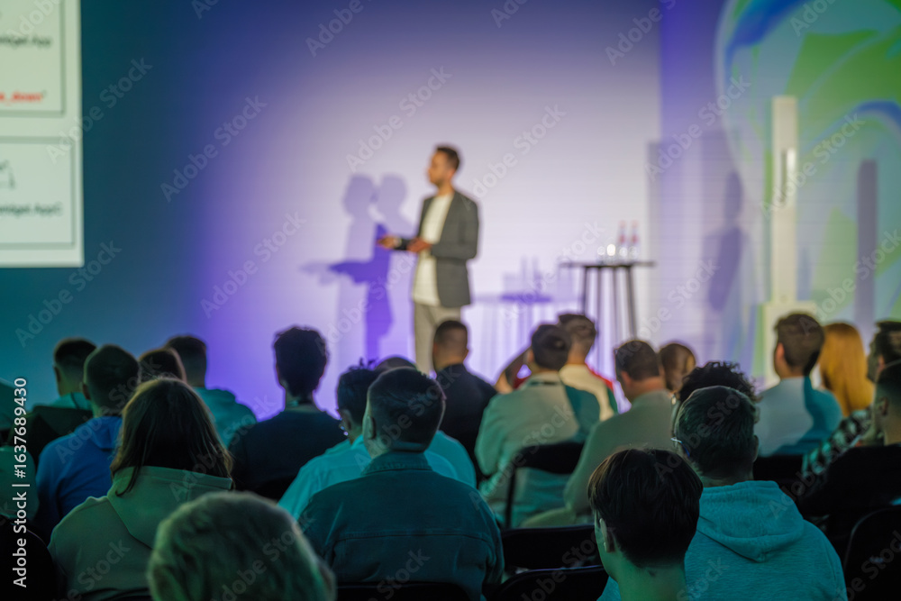 Obraz premium Professional speaker delivering presentation to audience in a modern conference setting with vibrant environment and engaging atmosphere