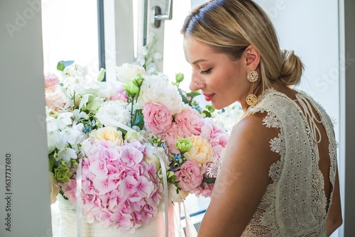 Φωτογραφία A beautiful and happy young woman in an elegant festive outfit enjoys the delicate aroma of a bouquet of flowers placed on a windowsill