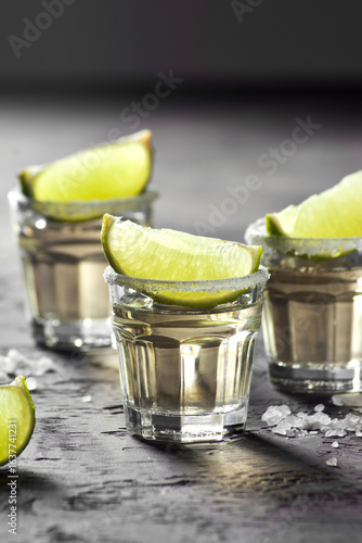 Refreshing tequila shots served in clear glasses with lime wedges on the rim, garnished with coarse salt, creating a vibrant and festive atmosphere for social gatherings