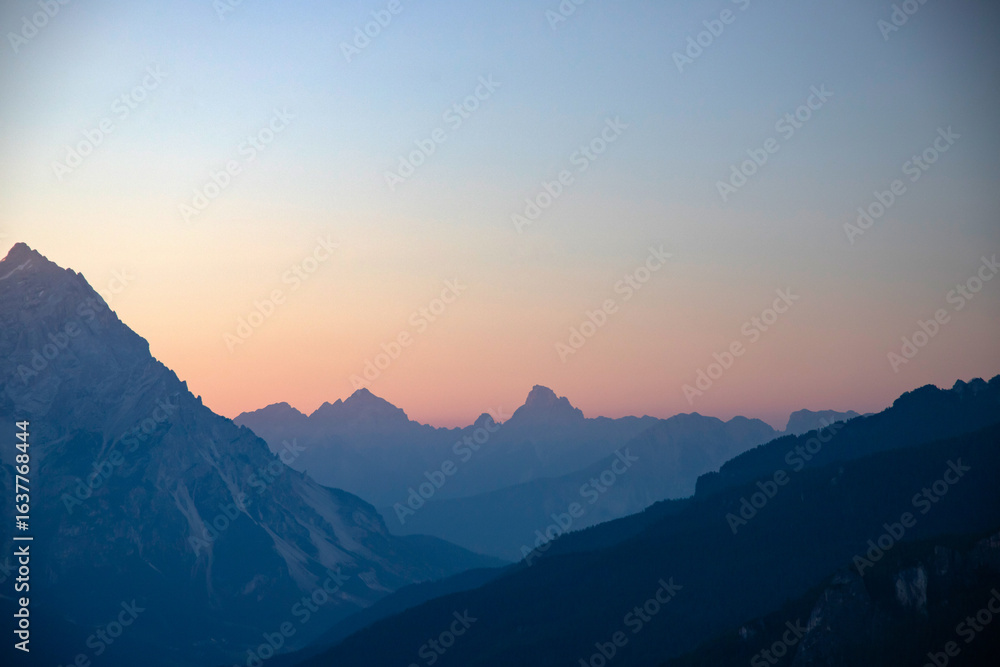 Fototapeta premium Distant mountain peaks layers at sunrise. Pattern of mountains silhouettes against orange sky in Dolomites.