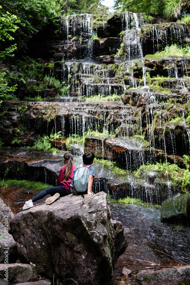 Fototapeta premium Young hikers admiring cascading waterfall in lush forest