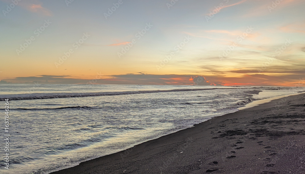 Fototapeta premium Tropical beach sunset with golden sky, gentle waves and serene ocean horizon view