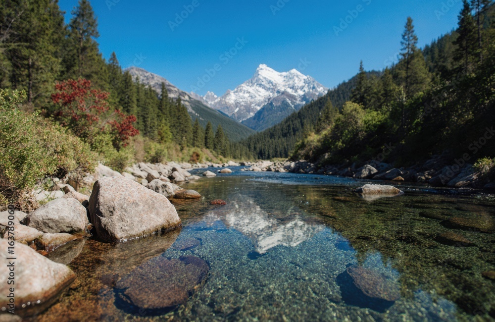 Fototapeta premium A clear mountain river flows through a lush green forest with snow-capped peaks in the background