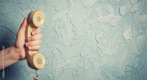 Hand Holding an Old-Fashioned Telephone Receiver Against a Textured Blue Wall Backdrop for Communication Concepts