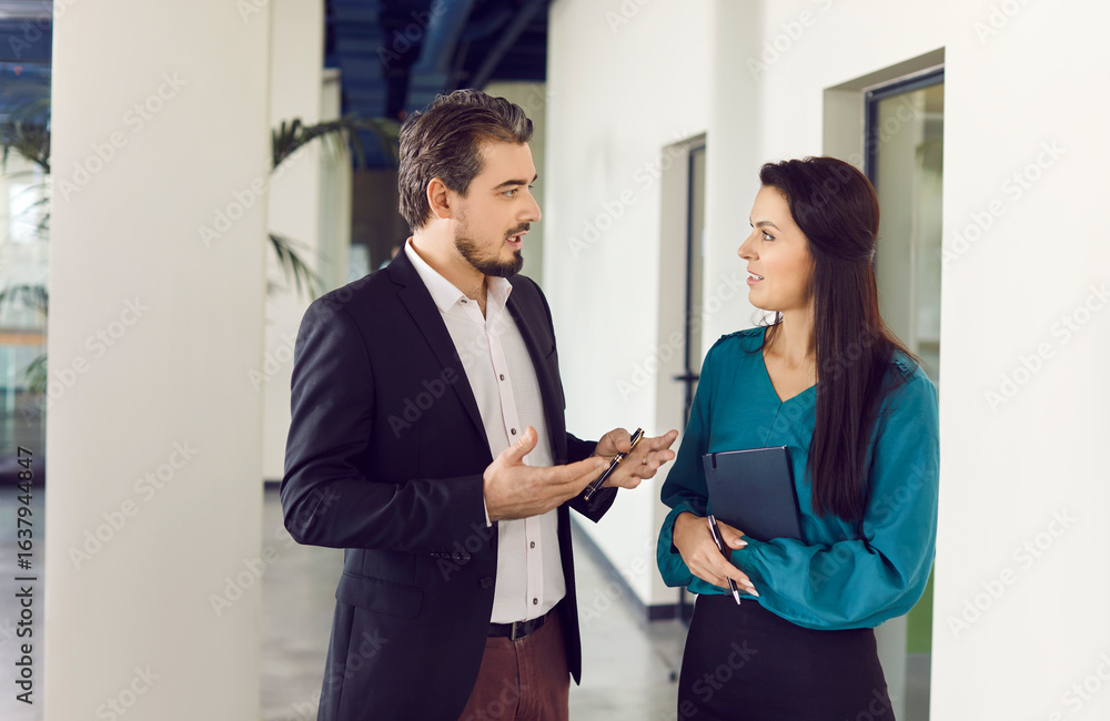 Fototapeta premium Colleagues, a man and a woman, engaged in discussion, talking during office work meeting. Teamwork and collaboration, open communication and working together in a business environment.