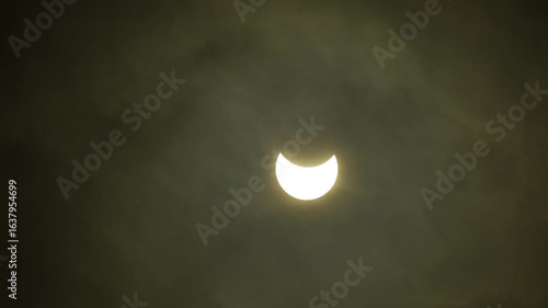 Partial solar eclipse captured through drifting clouds in daytime sky. Solar eclipse is mysterious natural phenomenon when Moon passes between planet Earth and Sun