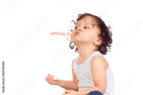 Cute curly haired toddler brushing his teeth with toothbrush and toothpaste