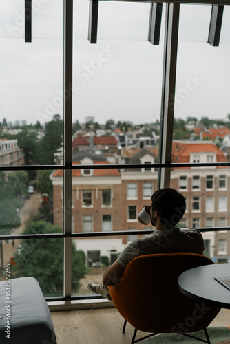 Canvas Print man drinking coffee in a chair with attic window and view on Amsterdam