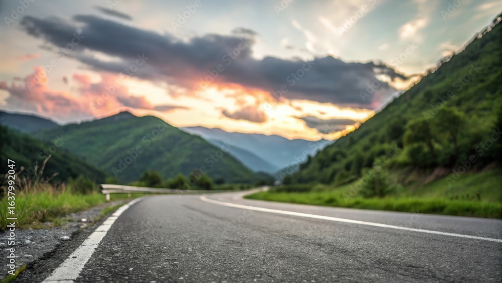 Naklejka premium Asphalt road square bordered by green mountain — colorful sunrise with scattered clouds above