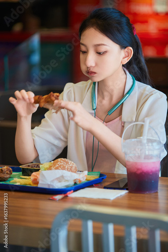 A cute Chinese girl enjoying a hearty meal at a fast-food restaurant in a shopping mall.