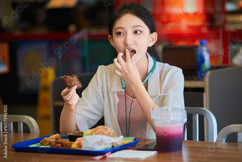 Konstfotografi A cute Chinese girl enjoying a hearty meal at a fast-food restaurant in a shopping mall