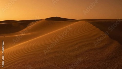 The desert at the sun - the vast desert is full of golden sand dunes when the sunset. The sand waves are stretched under the orange sky in the evening. The soft wind blows the sand to create smooth wr