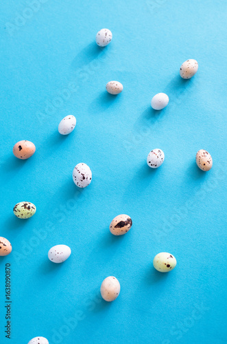 An arrangement of small, colorful, speckled eggs displayed randomly on a vibrant blue backdrop
