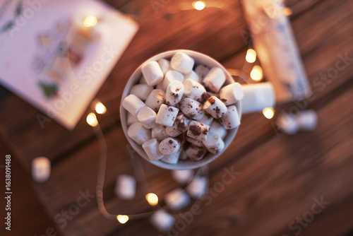 A cozy depiction of a hot beverage topped with marshmallows, surrounded by warm lights, invoking feelings of comfort and holiday spirit. Perfect for themes of winter, warmth, or festive occasions.