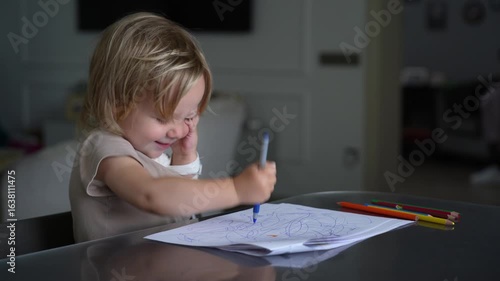 Blond child or toddler is engrossed in drawing and scribbling on paper with pens, pencils, and crayons, showing intense concentration and creativity