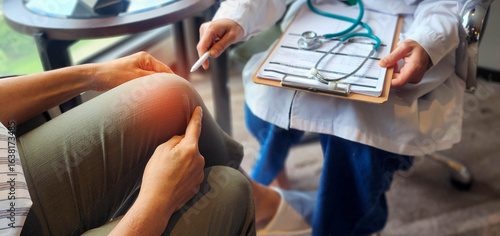 Patient showing knee pain to a doctor holding a clipboard and stethoscope, during a medical consultation for joint injury or arthritis treatment in a bright clinic setting