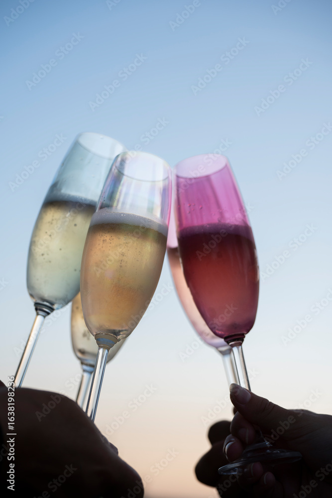 Obraz premium Champagne flutes are raised in a toast as friends gather at sunset, enjoying sparkling drinks and each other's company against a vibrant evening sky.