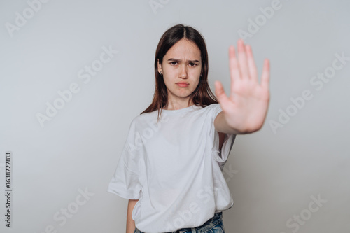 Wallpaper Mural A young woman with long hair wearing a white t-shirt and jeans stands against a plain background, extending her hand forward in a stop gesture, with a serious expression. Torontodigital.ca
