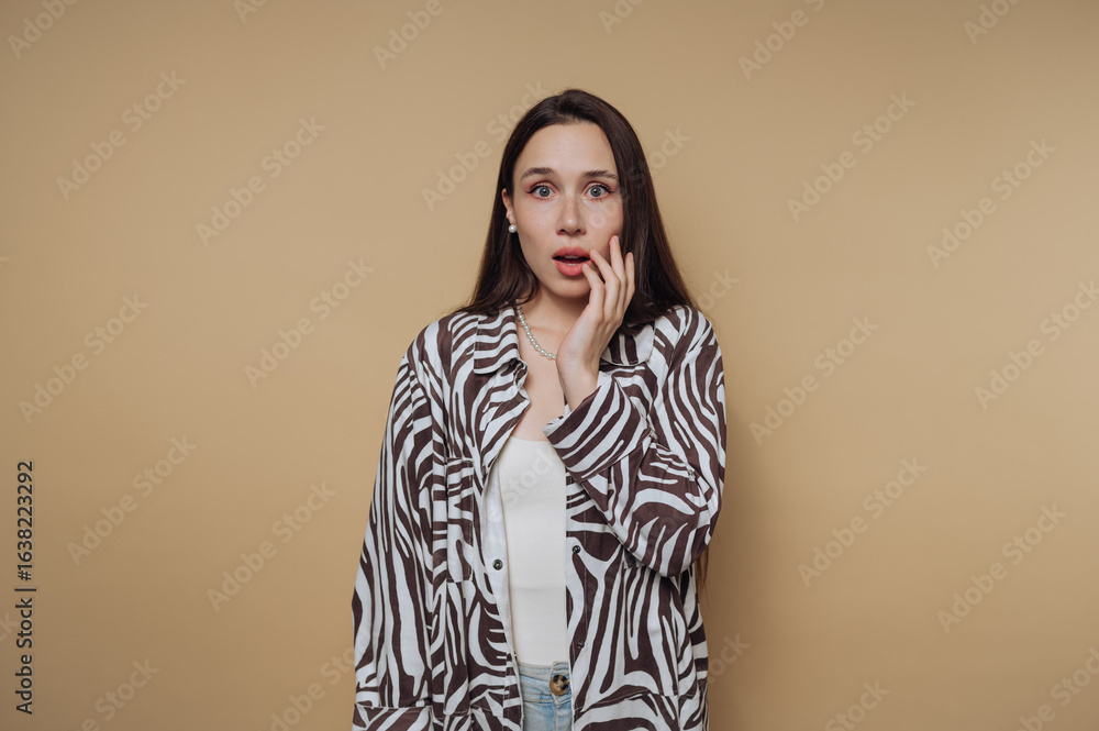 A surprised woman with long dark hair wearing a zebra-patterned shirt against a beige background. A surprised woman with long dark hair wearing a zebra-patterned shirt against a beige background.