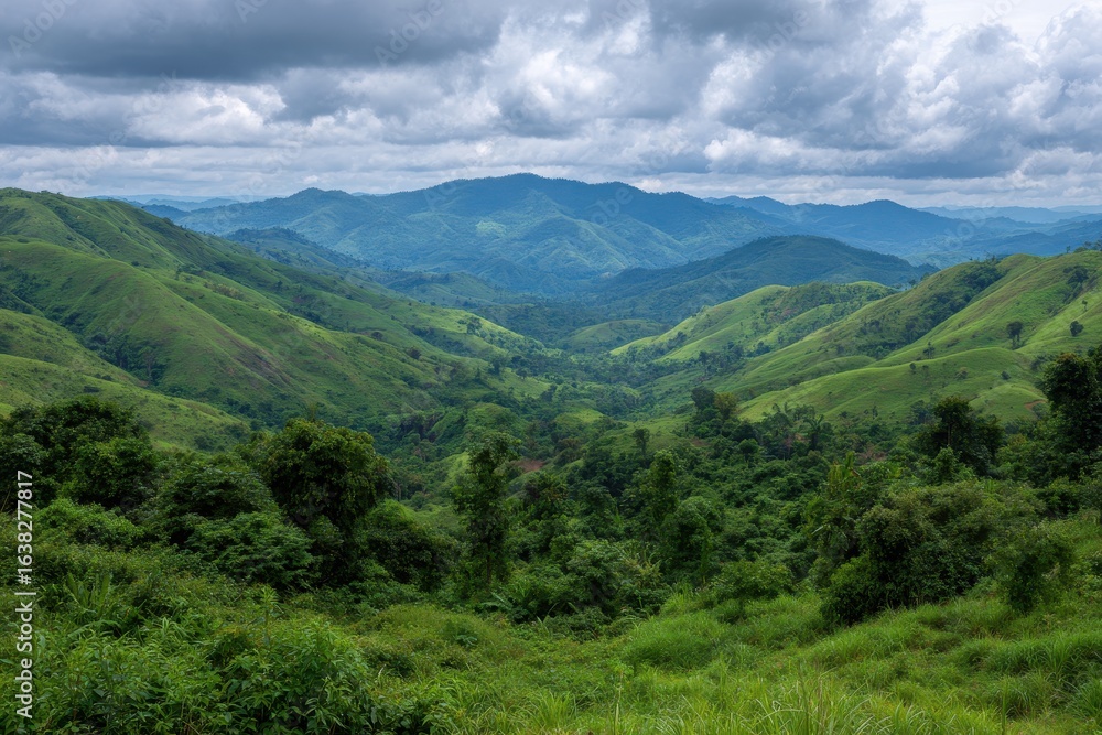 Naklejka premium Expansive lush green mountain range under a dramatic cloudy sky in a serene natural landscape