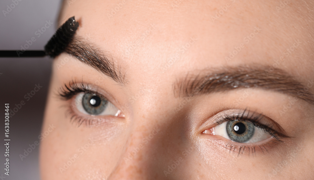 Naklejka premium Young woman brushing her eyebrow with spoolie on light grey background, closeup