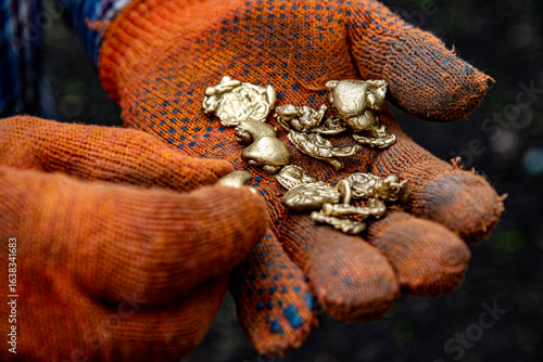 Foto Hands in work gloves holding pieces of gold nuggets