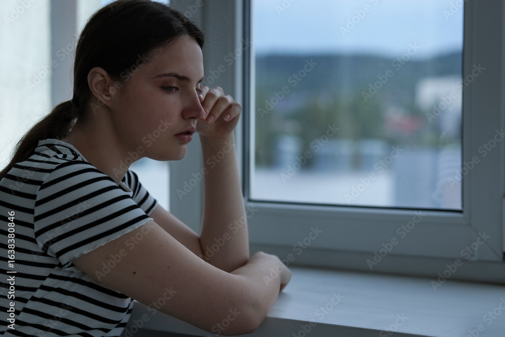 Sad young woman near window at home, space for text Sad young woman near window at home, space for text