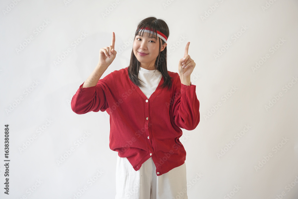 Φωτογραφία Joyful young woman in a red shirt and white pants is pointing to the copy space upwards, isolated white background