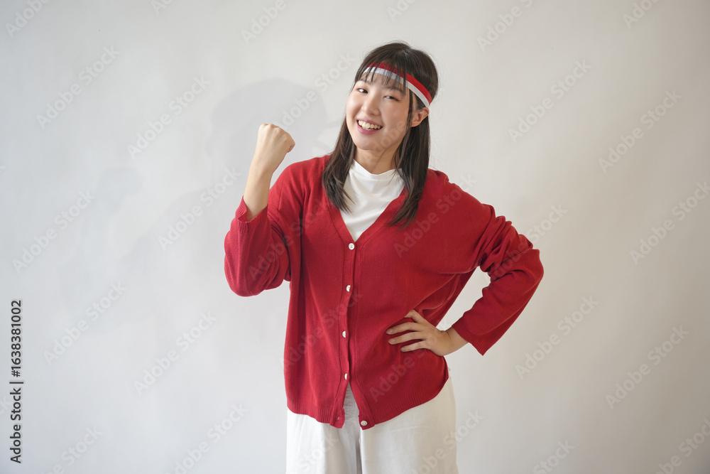 Φωτογραφία A cheerful young Asian woman in a red shirt and white pants smiles and raises her arms in the air to celebrate Indonesian independence