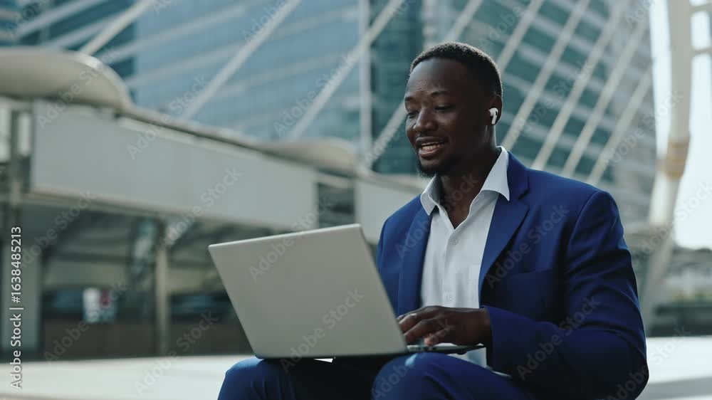 Portrait of positive African American businessman greets partners on video call via laptop on street. Man corporate employee joins video meeting sitting against skyscraper building Portrait of positive African American businessman greets partners on video call via laptop on street. Man corporate employee joins video meeting sitting against skyscraper building