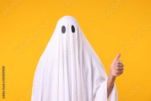 Фотография Man in ghost costume showing thumbs up on orange background