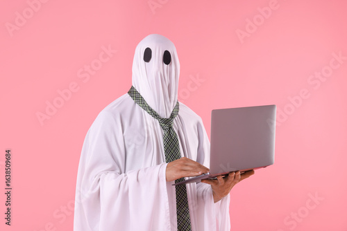 Obraz na płótnie Man in ghost costume using laptop on pink background
