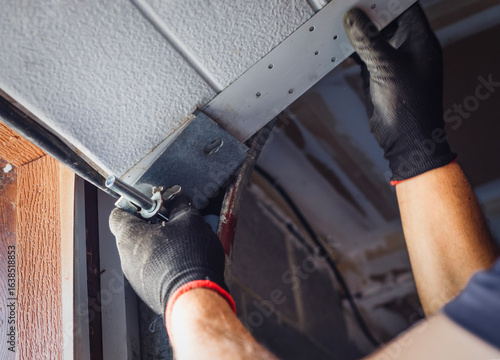 Fotografie Close-up of a worker attaching rollers to the metal tracks of a garage door during installation or repair