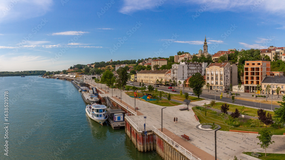 Fototapeta premium Panoramic view of Sava River from Brankov Bridge: boats, promenade, bike lane, historic buildings and St. Michael's Cathedral under summer sky. Belgrade, Serbia.