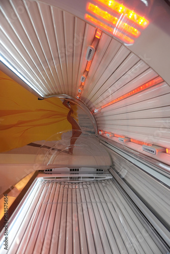 Inside solarium tanning bed with UV lamps and red light beauty salon background