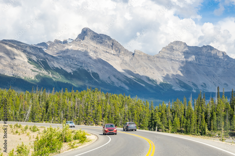 Fototapeta premium Car driving along Icefields Parkway toward towering Rocky Mountains