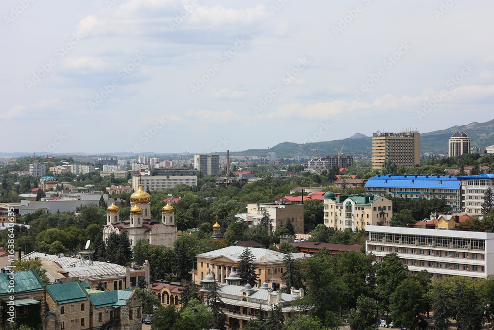 Naklejka premium Aerial View Of Pyatigorsk City, A Spa Resort Town In Russia, With The Golden Domes Of Spassky Cathedral And Caucasus Mountains In The Background.
