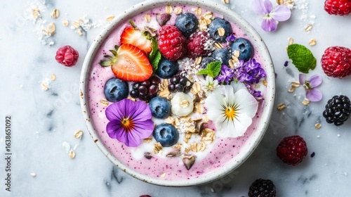 Overhead view of colorful smoothie bowl with edible flowers, seeds, and fresh berries on marble surface -