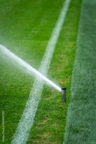 Automatic sprinkler watering green grass on soccer field