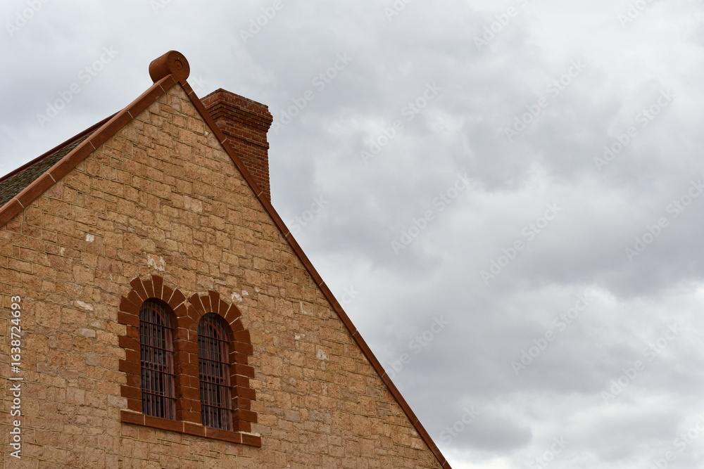 Fototapeta premium Classic stone building with red brick chimney against cold gray sky.