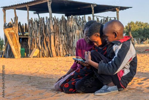 Фотография group of three african kids schooling on the phone in the village, taking online
