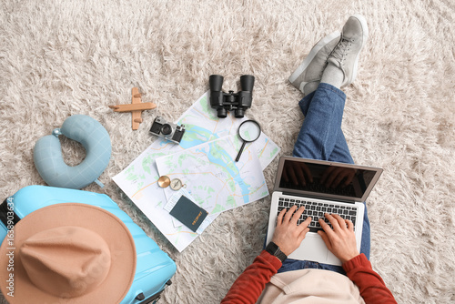 Young male tourist with map, laptop and suitcase planning his trip at home, t...