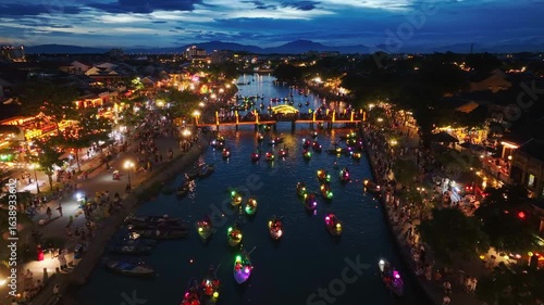 Aerial view of Hoi An city at night in Quang Nam province, Vietnam, a popular tourist destination, with colorful lantern-lit boats sailing along the river.
