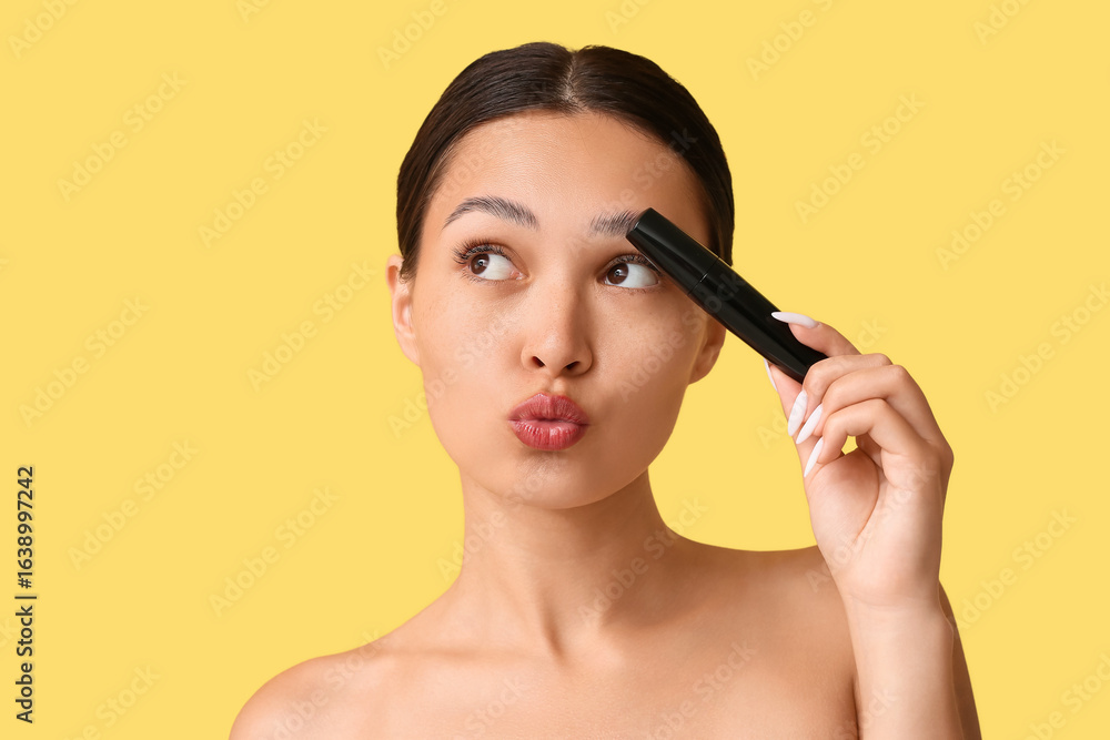 Fototapeta premium Beautiful young Asian woman with mascara blowing kiss on yellow background