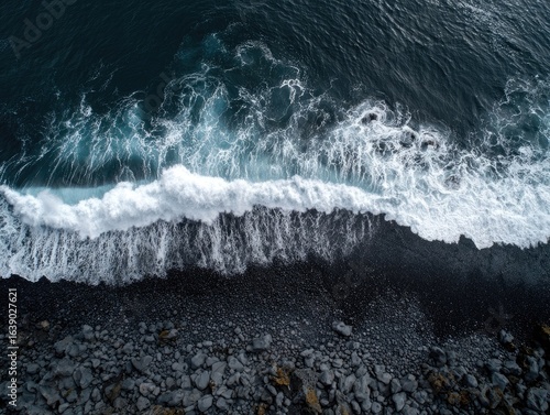 High-angle view of dark volcanic beach meeting dark ocean waves