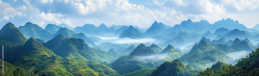 Fototapeta premium Expansive panoramic view of lush green mountainous landscape with mist and clouds creating a serene and tranquil atmosphere