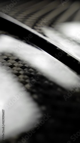 Extreme close-up macro video of abstract, pristine, high-tech dark metallic surface, polished black carbon fiber reflecting studio light, revealing a delicate curve, emphasizing advanced materiality